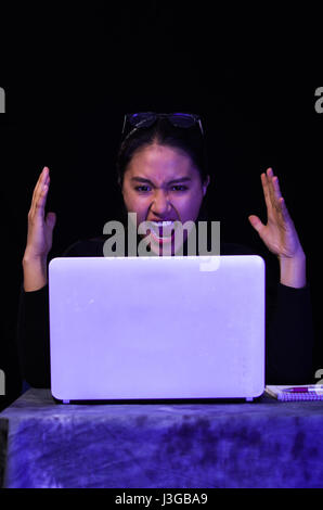 Bella ragazza urlando di fronte il suo laptop su sfondo scuro Foto Stock