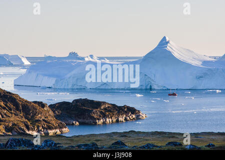 Una nave di fronte a un gigantesco iceberg in Groenlandia Foto Stock