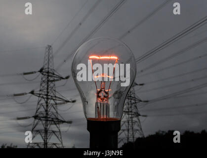 Rete elettrica ad alta tensione sulle linee di alimentazione al tramonto con un filamento illuminato in una lampadina incandescente in Scozia centrale Foto Stock