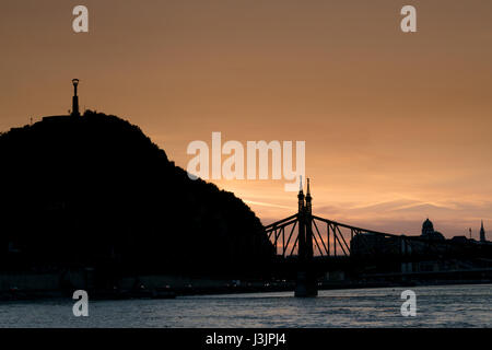 Con il sole che tramonta sulla Budapest il Ponte Elisabetta e la Statua della Libertà si stagliano dalla luce dorata. Foto Stock