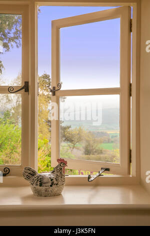 La luce del mattino che mostra attraverso un paese di lingua inglese cottage finestra dove un pollo di ceramica si siede a guardare la vista. Foto Stock