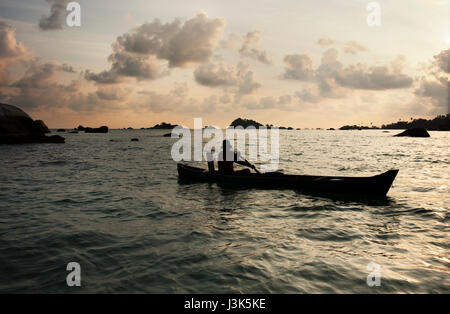 Silhouette di un uomo che rema con una piccola barca con la sua pala sull'oceano al tramonto, belitung indonesia. Foto Stock