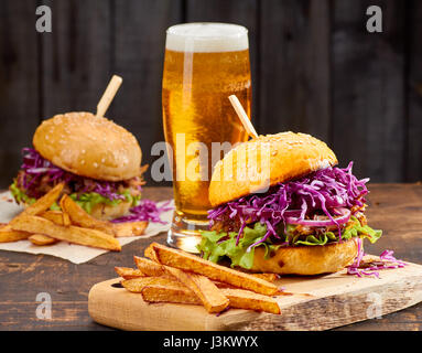 Due panini con estratto di carne di maiale, patatine fritte e un bicchiere di birra su sfondo di legno Foto Stock