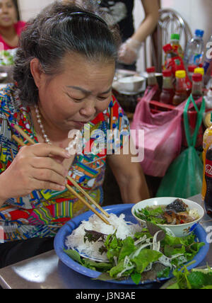 Donna vietnamita mangiare tagliatelle in una bancarella di strada di Hanoi, Vietnam Foto Stock