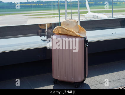 Una valigia con un cappello di paglia su di esso stare in aeroporto terrazza con un aereo su sfondo Foto Stock