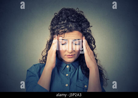 Triste closeup donna giovane con preoccupato ha sottolineato faccia avente espressione cefalea isolata sul muro grigio Sfondo. Le emozioni umane, salute mentale concetto Foto Stock