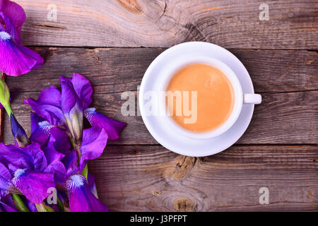 Tazza di caffè su un piattino accanto a un bouquet di viola iridi, vista dall'alto Foto Stock