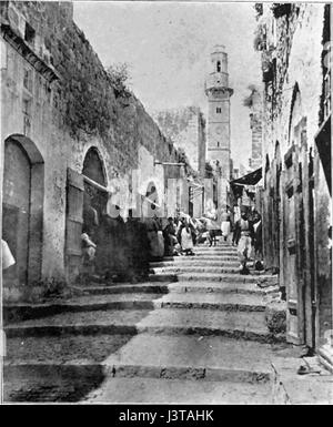 Una fotografia del 1906 della via dolorosa a Gerusalemme, che cattura i pellegrini che attraversano il percorso che si ritiene essere il percorso di Gesù verso la sua crocifissione. L'immagine offre uno sguardo storico sull'aspetto della strada e sulle pratiche devozionali del tempo. Foto Stock