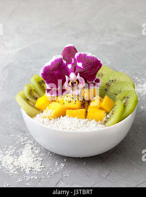 Insalata di mango, kiwi, scaglie di noce di cocco in una ciotola bianco su un cemento grigio sfondo Foto Stock