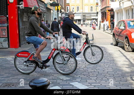 Due uomini turisti maschio ciclismo su Santander Biciclette Biciclette sul Wardour Street nel quartiere di Soho Londra UK KATHY DEWITT Foto Stock