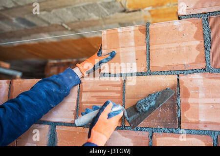 Muratore lavoratore installazione di muratura di mattoni sulla parete esterna con cazzuola spatola Foto Stock