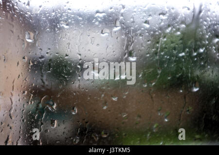 La pioggia contro la finestra che guarda al giardino e case. Foto Stock