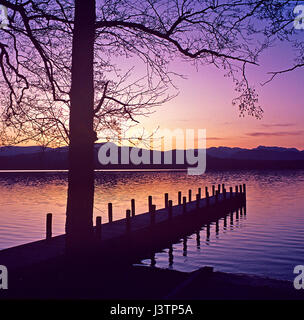 Un iconico tramonto sul Lago di Windermere nel distretto del lago con una vista stupenda attraverso il profilarsi di alberi per le lontane colline Foto Stock