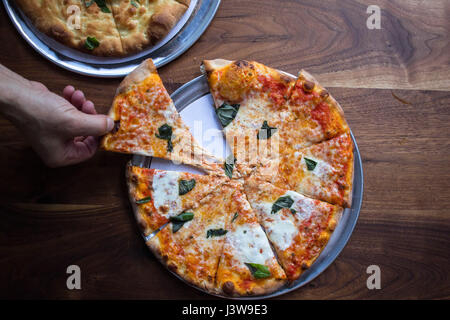 Un uomo di prendere una fetta di pane appena sfornato brick oven pizza Foto Stock