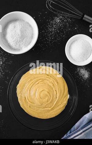 Base torta fatta in casa o pasta biscotto in recipiente di vetro con gli ingredienti sul lato, fotografato overhead su ardesia con luce naturale Foto Stock