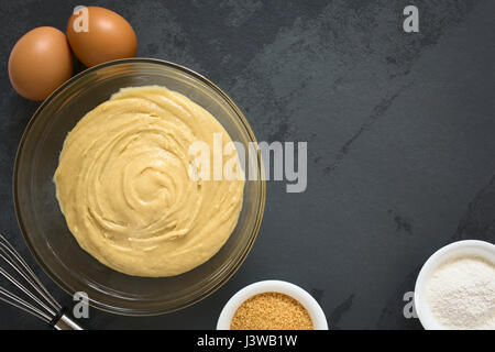 Base torta fatta in casa o pasta biscotto in recipiente di vetro con ingredienti e mescolare con una frusta sul lato, fotografato overhead su ardesia con luce naturale Foto Stock