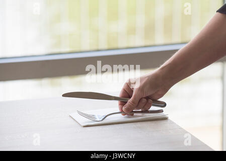 Posate poste su un tavolo in un ristorante di coltello e forchetta tovagliolo tovagliolo Impostazione di una tabella cameriera Hand Arm Foto Stock