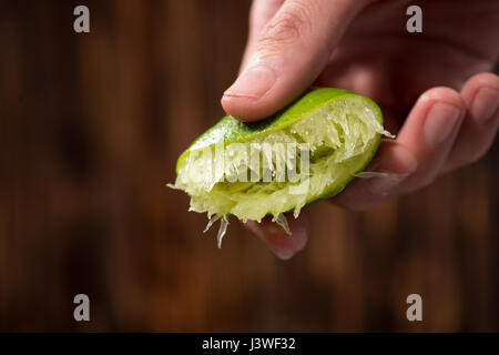 Schiacciare a mano calce con lime drop su scuro dello sfondo in legno Foto Stock