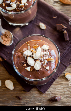 Un sano materie vegano Mousse al cioccolato guarnita con mandorle in bicchieri su sfondo in legno close up - deliziosa casa materie vegane budino di cioccolato con Foto Stock