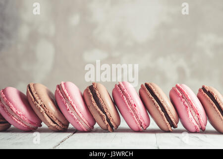 Fila di lampone e cioccolato color pastello Macarons o amaretti su calcestruzzo sfondo di pietra Foto Stock