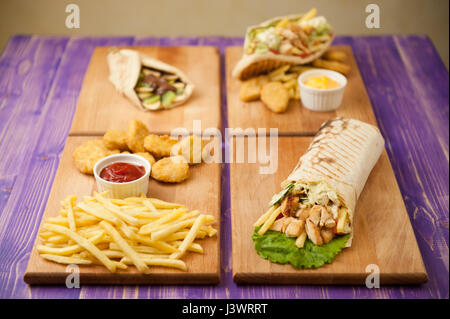 Patate fritte e pepite, shawarma arabo, greco il giroscopio e pita con cioccolato e kiwi con due tazze di formaggio e ketchup su quattro assi di legno su un Foto Stock