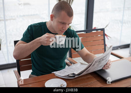 Giovane uomo si rilassa durante una pausa di lavoro. Legge le ultime notizie nel quotidiano e di bere il caffè. Foto Stock