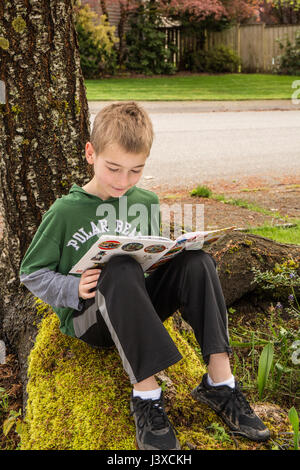 Bambino di nove anni la lettura di un libro all'ombra di un albero in Issaquah, Washington, Stati Uniti d'America Foto Stock