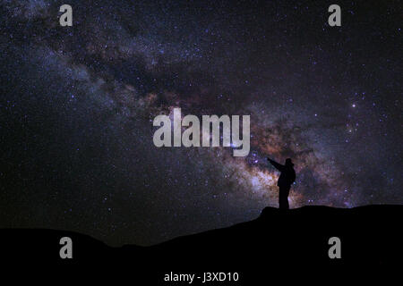 Un uomo è in piedi accanto alla via lattea puntando su una stella luminosa, una lunga esposizione fotografia, con grano Foto Stock