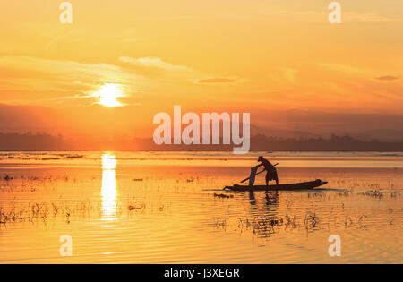 Silhouette pescatore sulla barca da pesca impostazione net con sunrise Foto Stock