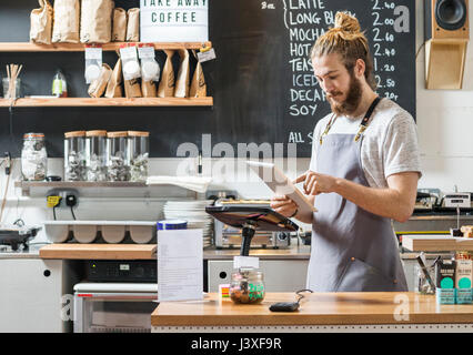 Giovane uomo dietro un contatore in un cafe utilizzando una compressa Foto Stock