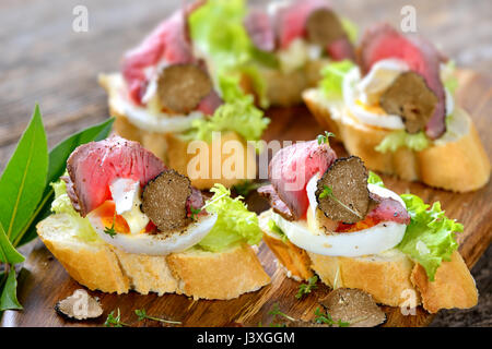 Crostini con un arrosto di manzo, nero autunno tartufi, Francese Formaggio Brie su una fetta di uovo sulla baguette con una foglia di insalata Foto Stock