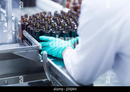 I lavoratori di disporre bottiglie sul nastro trasportatore sulla linea di produzione in impianto farmaceutico, metà sezione Foto Stock