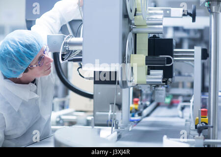 Lavoratore macchinari operativi sulla linea di produzione in stabilimento farmaceutico Foto Stock