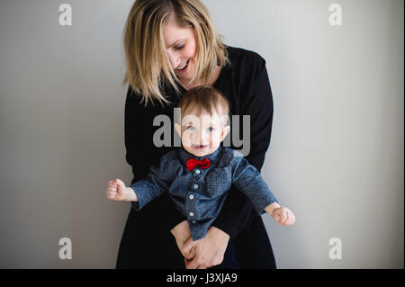 Ritratto di bimbi maschio in rosso il filtro bow tie essendo tenuto dalla madre Foto Stock