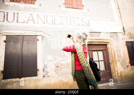 Donna prendendo fotografia di insegne su esterno dell'edificio, Bruniquel, Francia Foto Stock