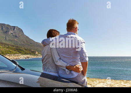 Giovane appoggiata sul cofano auto, guardando a vista costiera, vista posteriore, Città del Capo Foto Stock