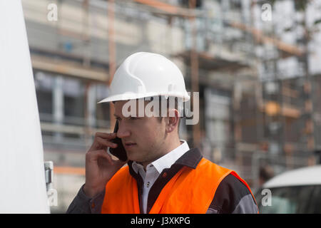 Giovane maschio ingegnere civile rendendo chiamata dello smartphone sul sito in costruzione Foto Stock