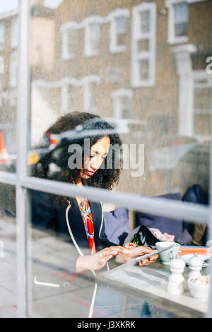La visualizzazione della finestra di donna con tavoletta digitale in cafe Foto Stock