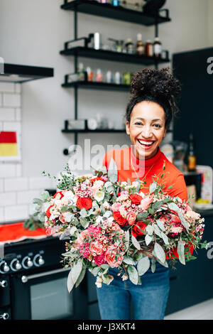 Ritratto di metà femmina adulta fioraio azienda bouquet di fiori in workshop per fioristi Foto Stock