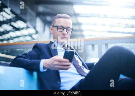 Imprenditore sul divano guardando lo smartphone nel atrio ufficio Foto Stock