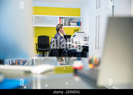 Uomo seduto alla scrivania in ufficio rendendo chiamata telefonica Foto Stock