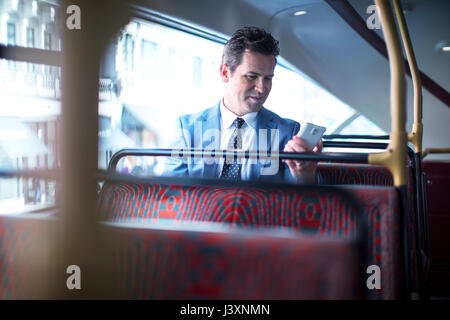 Imprenditore guardando smartphone sul double decker bus Foto Stock