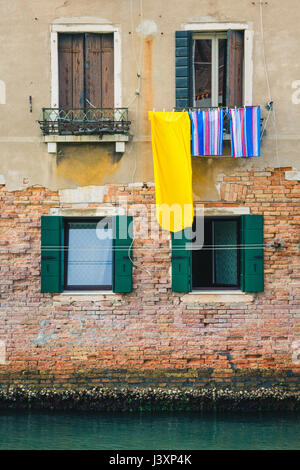 Lavanderia colorati appesi fuori da una finestra a Venezia, Italia con verdi acque della laguna sottostante. Foto Stock