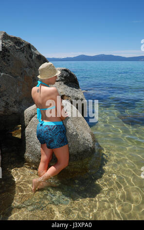 Una donna si appoggia contro una roccia su una spiaggia e si affaccia sul Lago Tahoe. Foto Stock