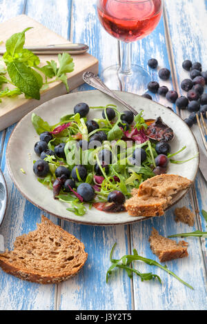 Una sana insalata con rucola e mirtilli su un tavolo esterno. Foto Stock