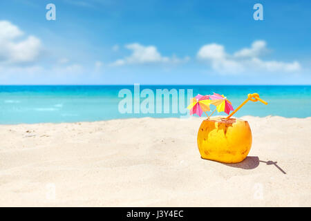 Cocktail di noce di cocco con paglia e ombrelloni colorati su una spiaggia, vacanze estate concetto, il fuoco selettivo, spazio per il testo. Foto Stock