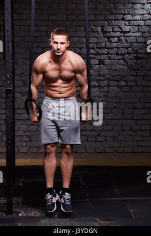 Fitness giovane uomo bello fare immersione esercizio utilizzando anelli contro un muro di mattoni in croce montare palestra. Foto Stock