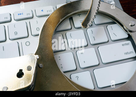 Online il concetto di criminalità. Manette sulla tastiera. Foto Stock