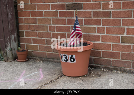 Vaso di fiori contro un muro di mattoni con il numero 136 su di essa e una piccola bandiera americana bloccata in esso Foto Stock