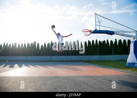 Giovane uomo di salto e facendo un fantastico Slam Dunk giocando stree Foto Stock